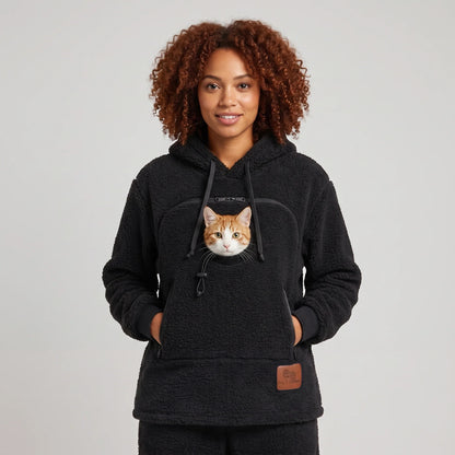 Woman wearing the black Dolgum Cozy Cat Hoodie with an orange and white cat in the front pouch