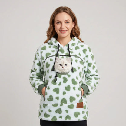 Woman wearing the green heart-print Dolgum Cozy Cat Hoodie with a white cat in the front pouch